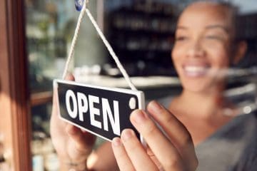 Happy business owner turning an open sign at a cozy coffee shop, welcoming customers.